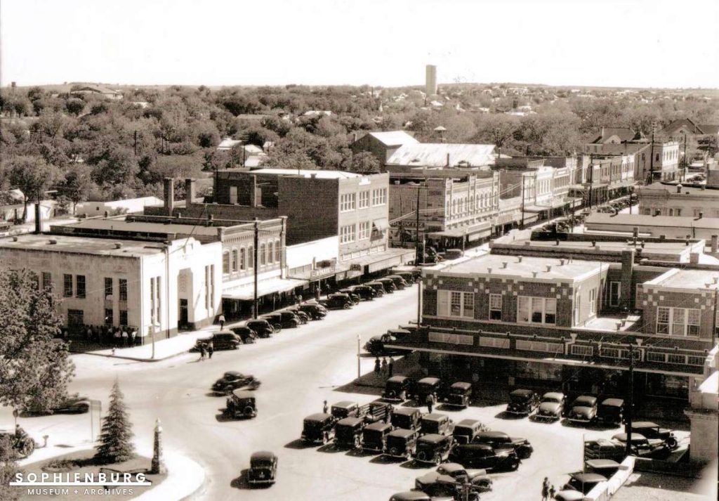 Photo Caption: April 1940 view of Main Plaza from the Comal County Courthouse bell tower. The white building on the left is the old First National Bank which has been wrapped with the red bricks of the Chase Bank building. Note that traffic can go either direction around the plaza.