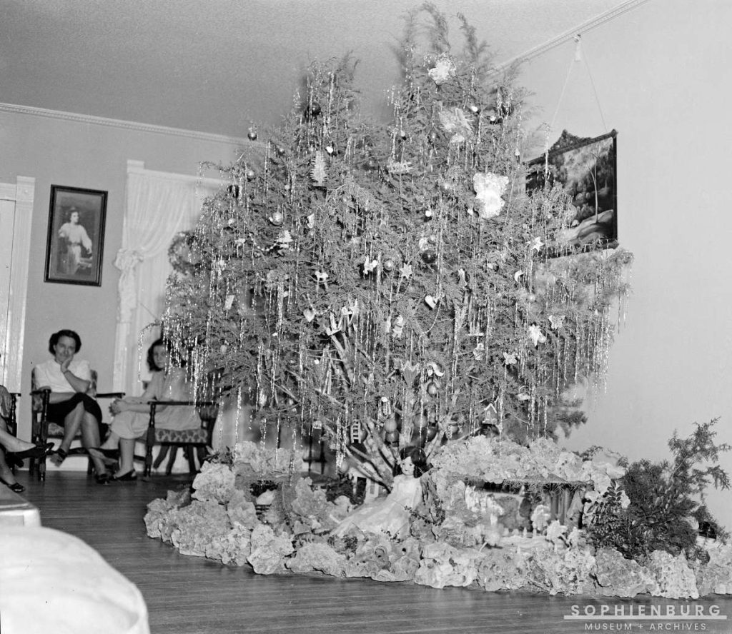 Photo Caption: The Seven Timmermann Sisters of Geronimo continued the tradition of a cut cedar from their pasture as their Christmas tree their entire lives. The photo shows their tree in 1947 decorated with tinsel, paper and tinsel ornaments, cookies and a few shiny balls; many of the ornaments dated back to the late 19th century. (S481-014)